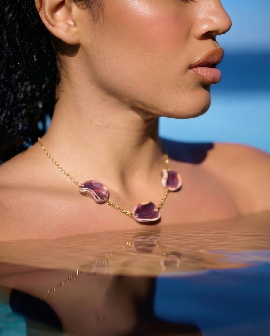 Woman wearing Akti plum ceramic necklace in the water, gold chain against sun-lit skin by the sea
