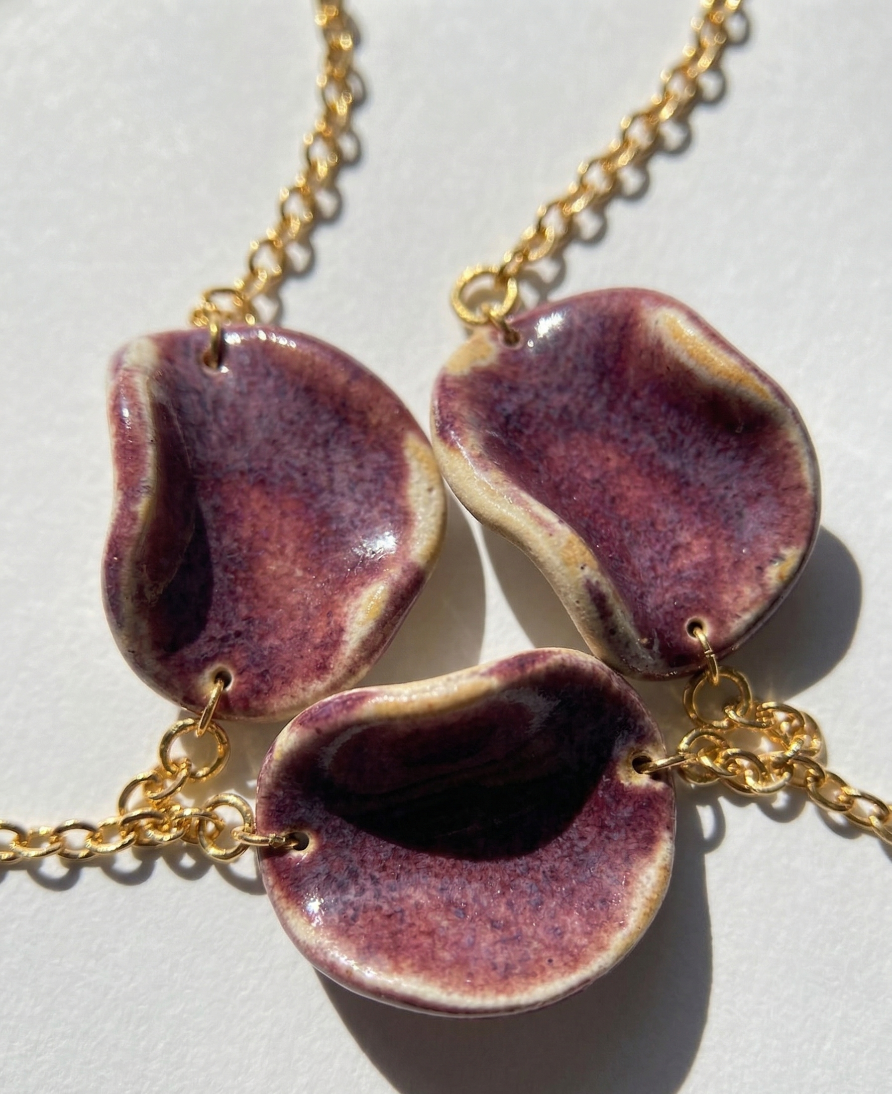 Akti plum ceramic necklace close up shot with gold chain, handmade organic petal forms in natural light 