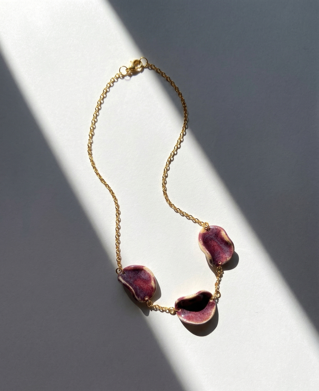 Akti plum ceramic necklace with gold chain, handmade organic petal forms in natural light and shadow