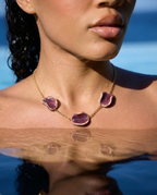 Woman wearing Akti plum ceramic necklace in the water, gold chain against sun-lit skin by the sea