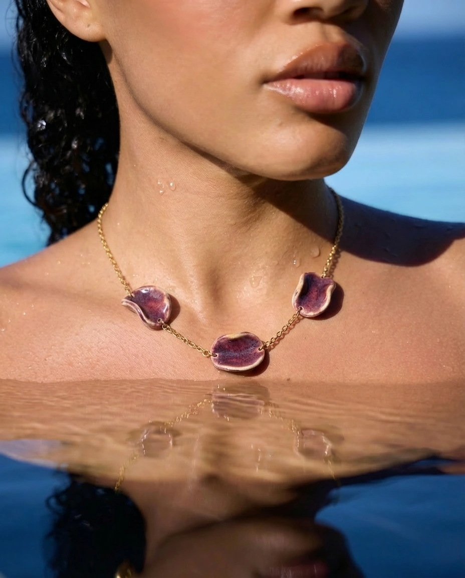Woman wearing Akti plum ceramic necklace in the water, gold chain against sun-lit skin by the sea