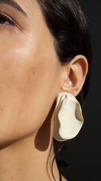 Woman wearing Anthi white ceramic statement earring, folded petal form in warm sunlight against skin