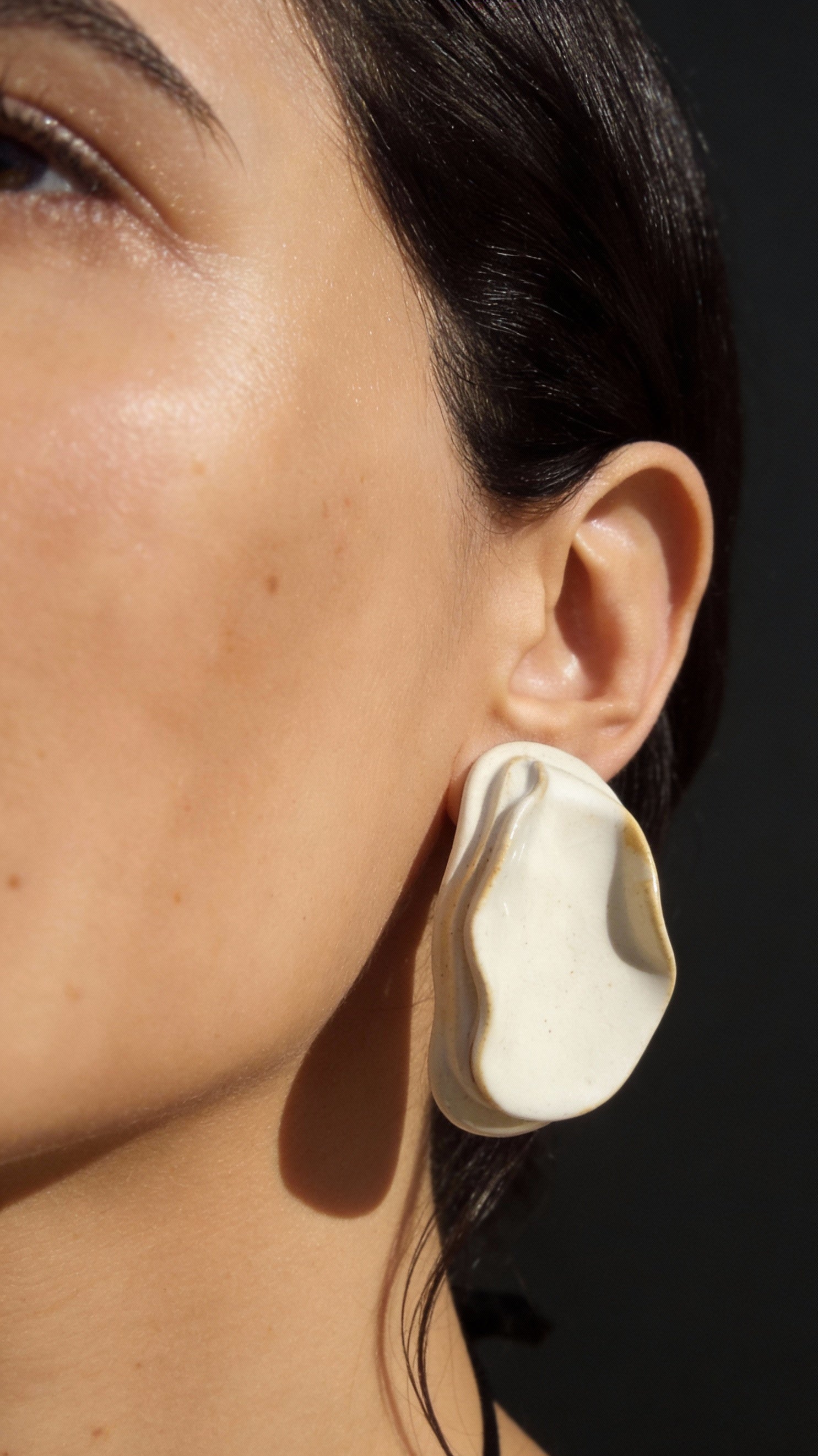 Woman wearing Anthi white ceramic statement earring, folded petal form in warm sunlight against skin