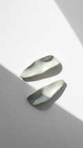 Galini ceramic statement earrings in white, handmade with organic wave-like form, shown in soft natural light and shadow