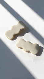 Two handmade ceramic jewelry with white white glaze and speckles, displayed diagonally on a white surface with dramatic window shadow patterns.